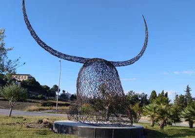 "Imponente escultura de hierro del Cap de Dimoni en la entrada de Santa Margalida, Mallorca." "Monumental obra del Cap de Dimoni, emblema de la tradición y la artesanía de Santa Margalida." "La Escultura del Cap de Dimoni en Santa Margalida, un punto de encuentro cultural en Mallorca." "Vista de la escultura del Cap de Dimoni en Santa Margalida, reflejo de las fiestas de la Beata." "El Cap de Dimoni de Santa Margalida, un hito artístico forjado en hierro en el corazón de Mallorca."