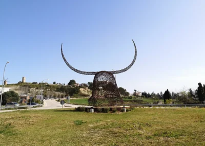 "Imponente escultura de hierro del Cap de Dimoni en la entrada de Santa Margalida, Mallorca." "Monumental obra del Cap de Dimoni, emblema de la tradición y la artesanía de Santa Margalida." "La Escultura del Cap de Dimoni en Santa Margalida, un punto de encuentro cultural en Mallorca." "Vista de la escultura del Cap de Dimoni en Santa Margalida, reflejo de las fiestas de la Beata." "El Cap de Dimoni de Santa Margalida, un hito artístico forjado en hierro en el corazón de Mallorca."